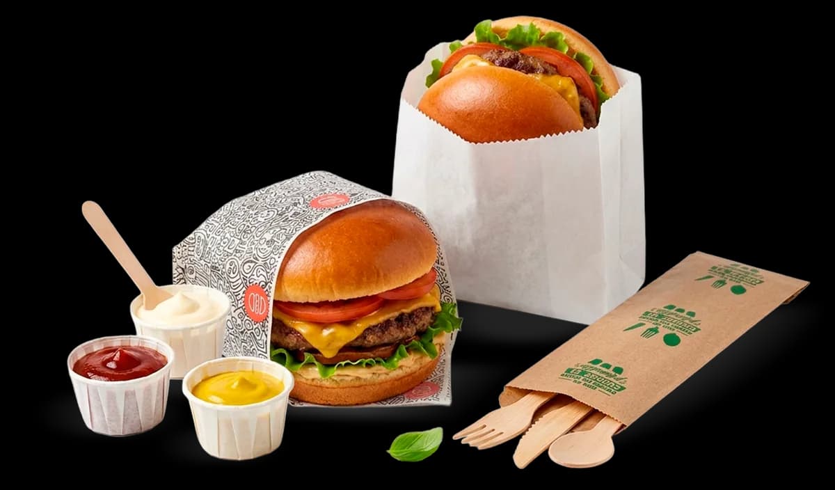 Hamburguesas envueltas en papel antigrasa, bolsas de papel y copas de salsa