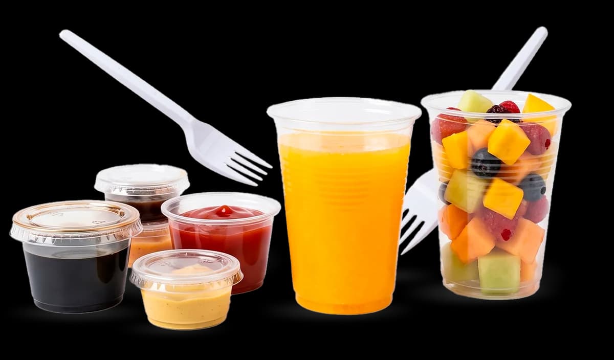 Vasos y copas plásticas con jugo, frutas y salsas